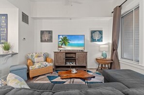 Una sala de estar con un sofá, una mesa de centro, un televisor y una mesita auxiliar.