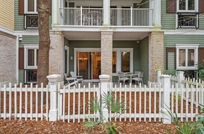 A two-story building with a white picket fence, a balcony, and outdoor seating area.