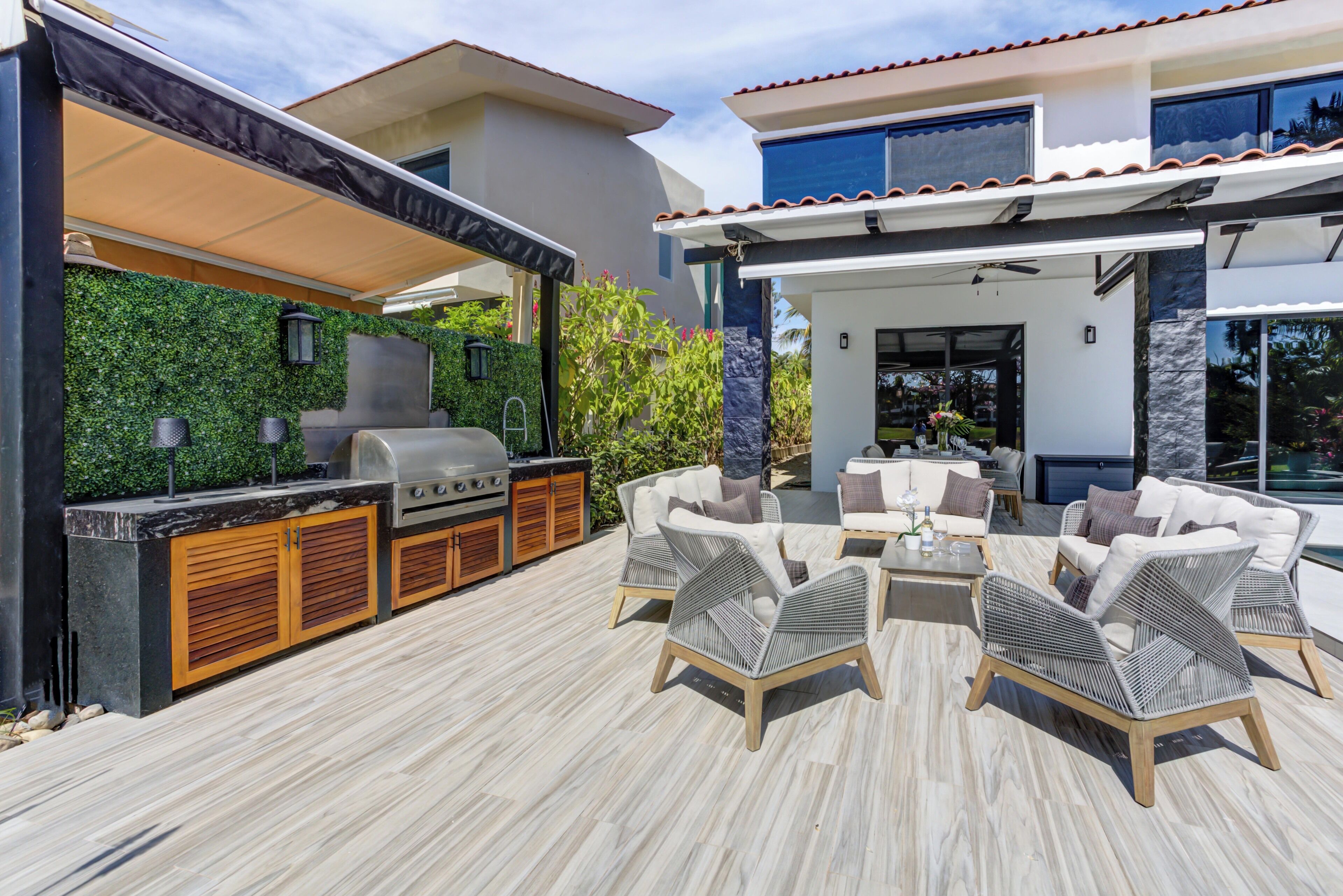 An outdoor patio with a grill, wicker furniture, and a green wall.
