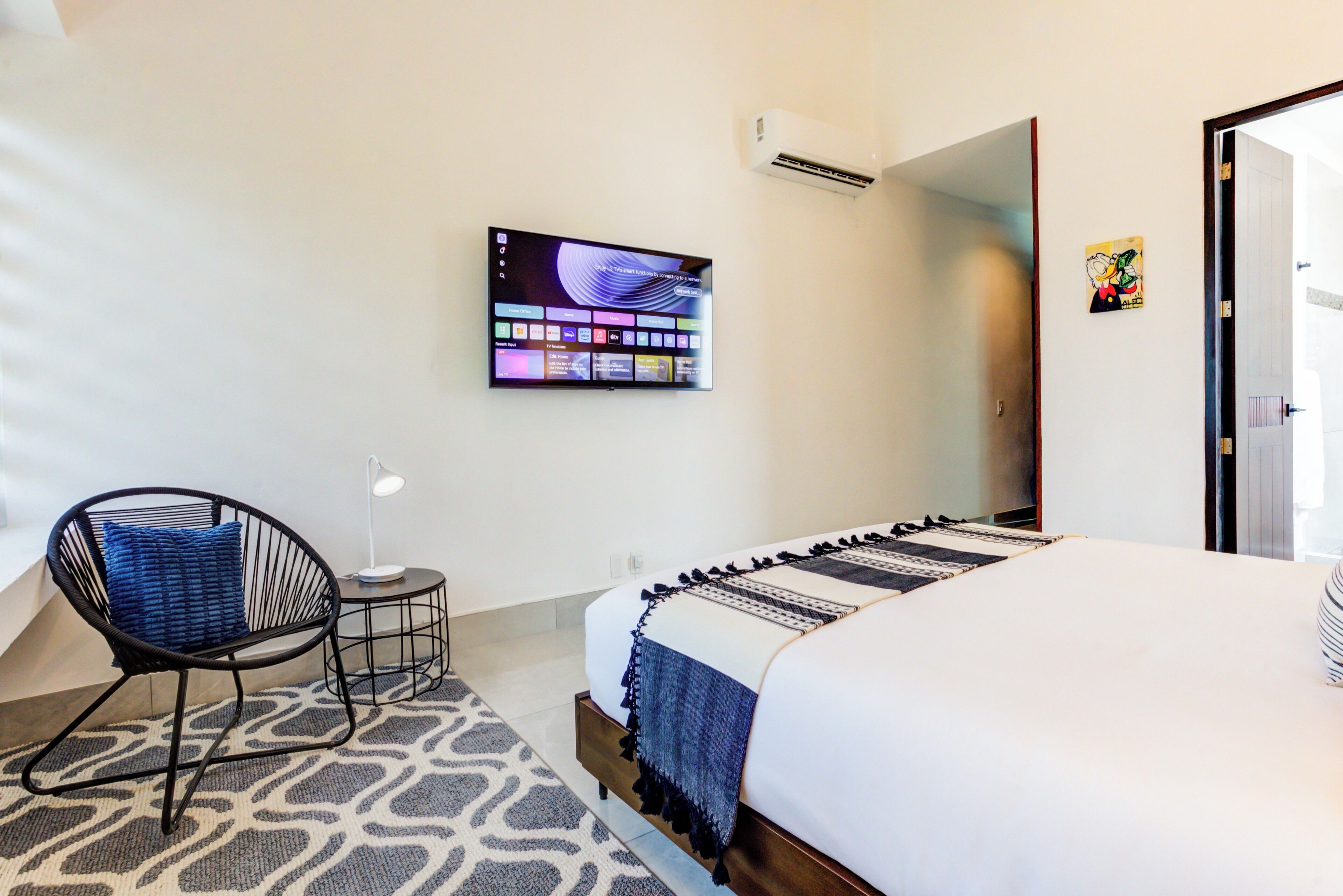 Une chambre d’hôtel avec un lit, une chaise, une petite table avec une lampe, un téléviseur fixé au mur et une porte.