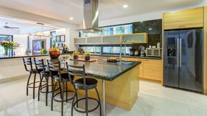 Una cocina moderna con una isla central, taburetes de bar, un refrigerador de acero inoxidable y un microondas.
