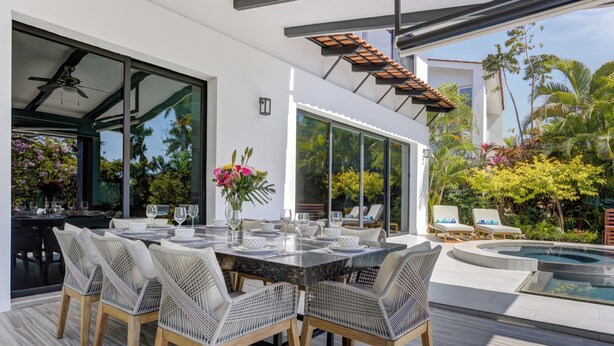 Un espacio moderno para comer al aire libre con una mesa grande, sillas de mimbre y una piscina.