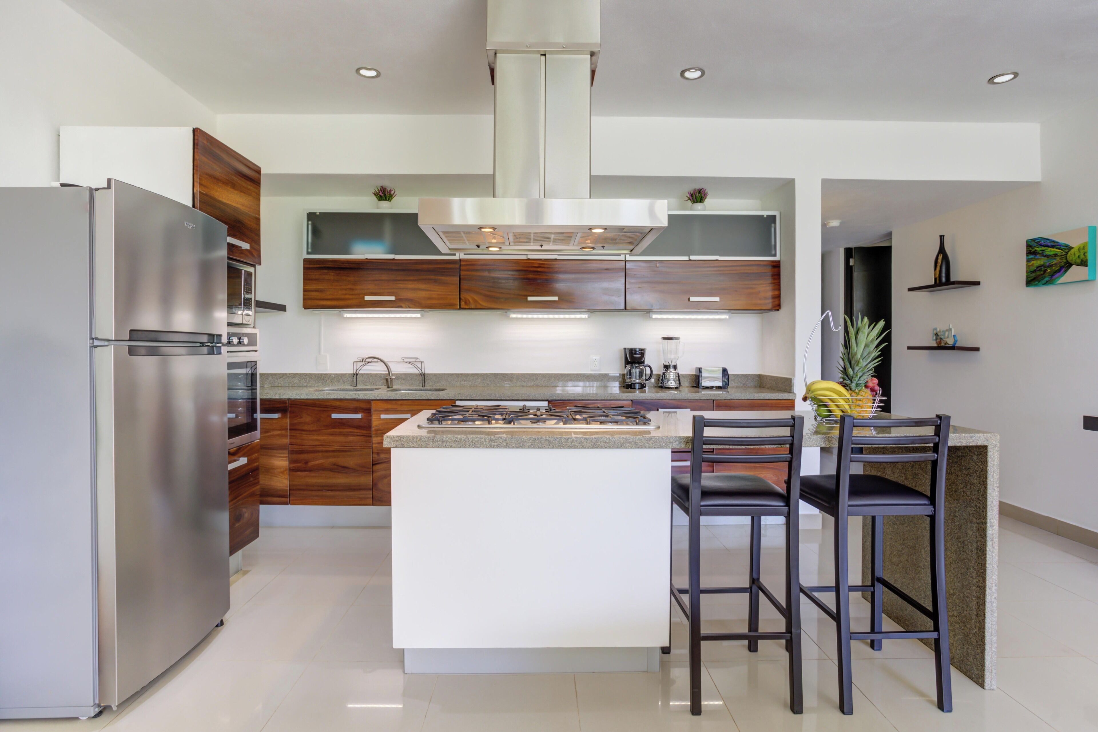 A modern kitchen with a central island, stainless steel appliances, wooden cabinets, and a gas stove.
