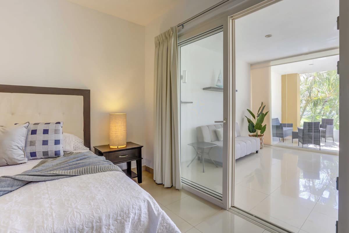 Een hotelkamer met een bed, een nachtkastje, een lamp en een schuifdeur naar een balkon met tuinmeubilair.