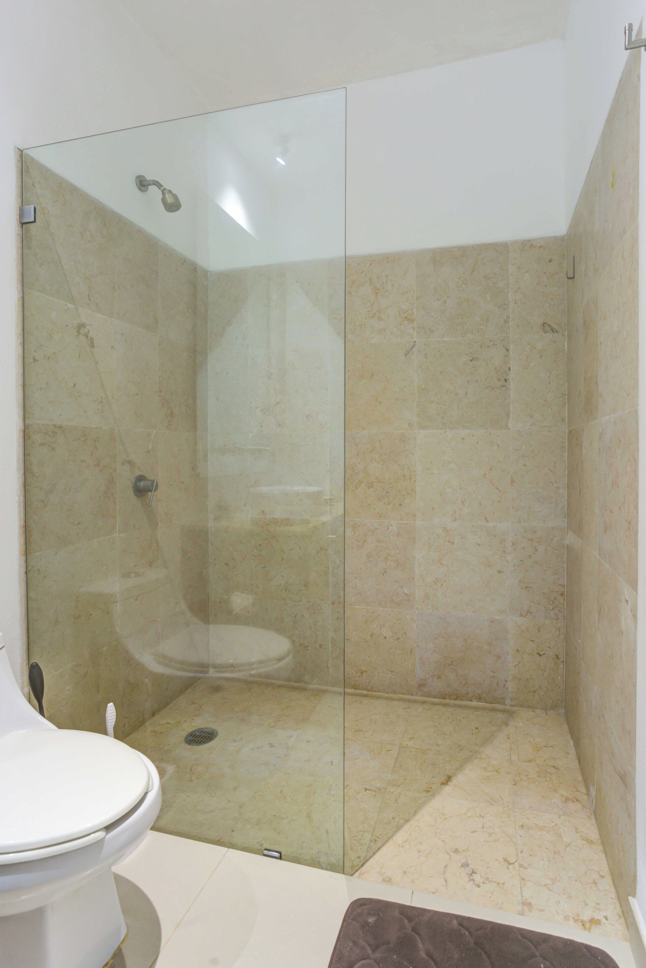 A bathroom with a glass-enclosed shower, a toilet, and beige tiled walls.