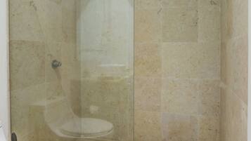 Ein Badezimmer mit Duschkabine, Toilette und beige gefliesten Wänden.