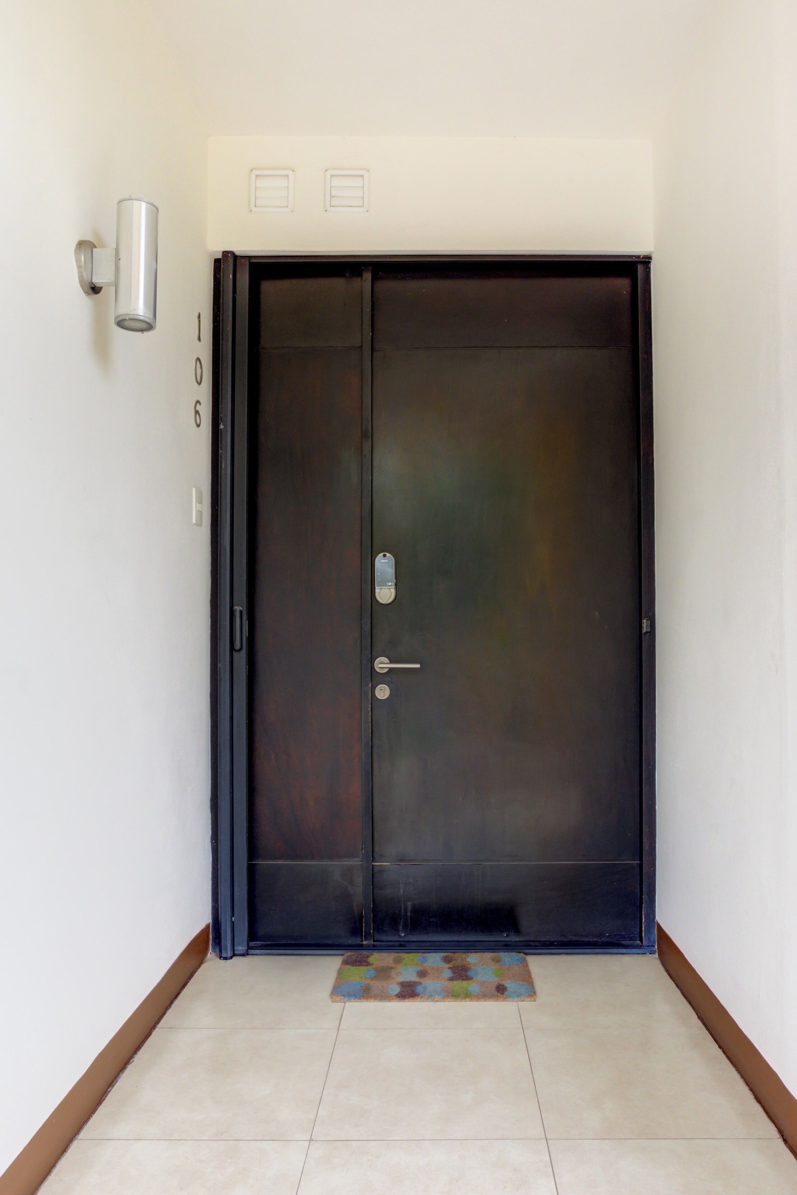Une porte fermée, de couleur sombre, dotée d’une poignée et d’un trou de serrure, ainsi qu’un interrupteur et un petit luminaire fixé au mur, situé juste au-dessus.