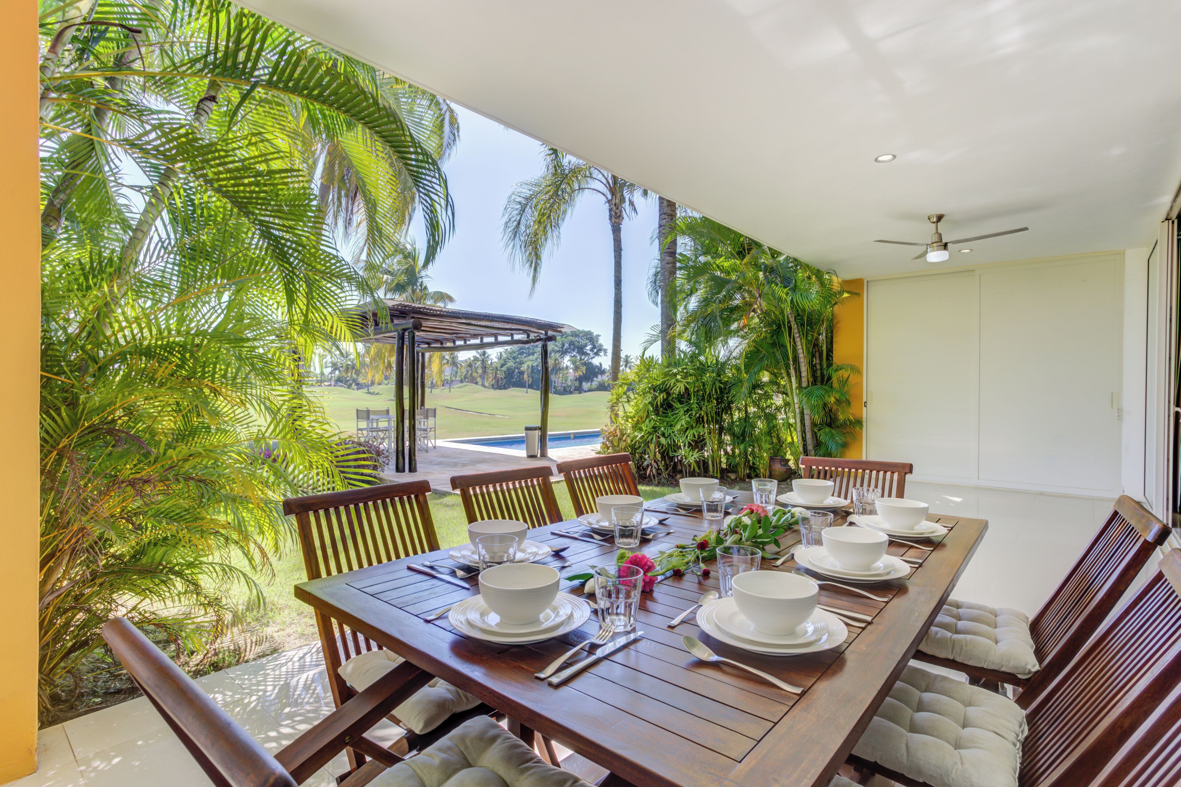 A dining area with a table set for six, surrounded by chairs, and a view of palm trees and a golf course.