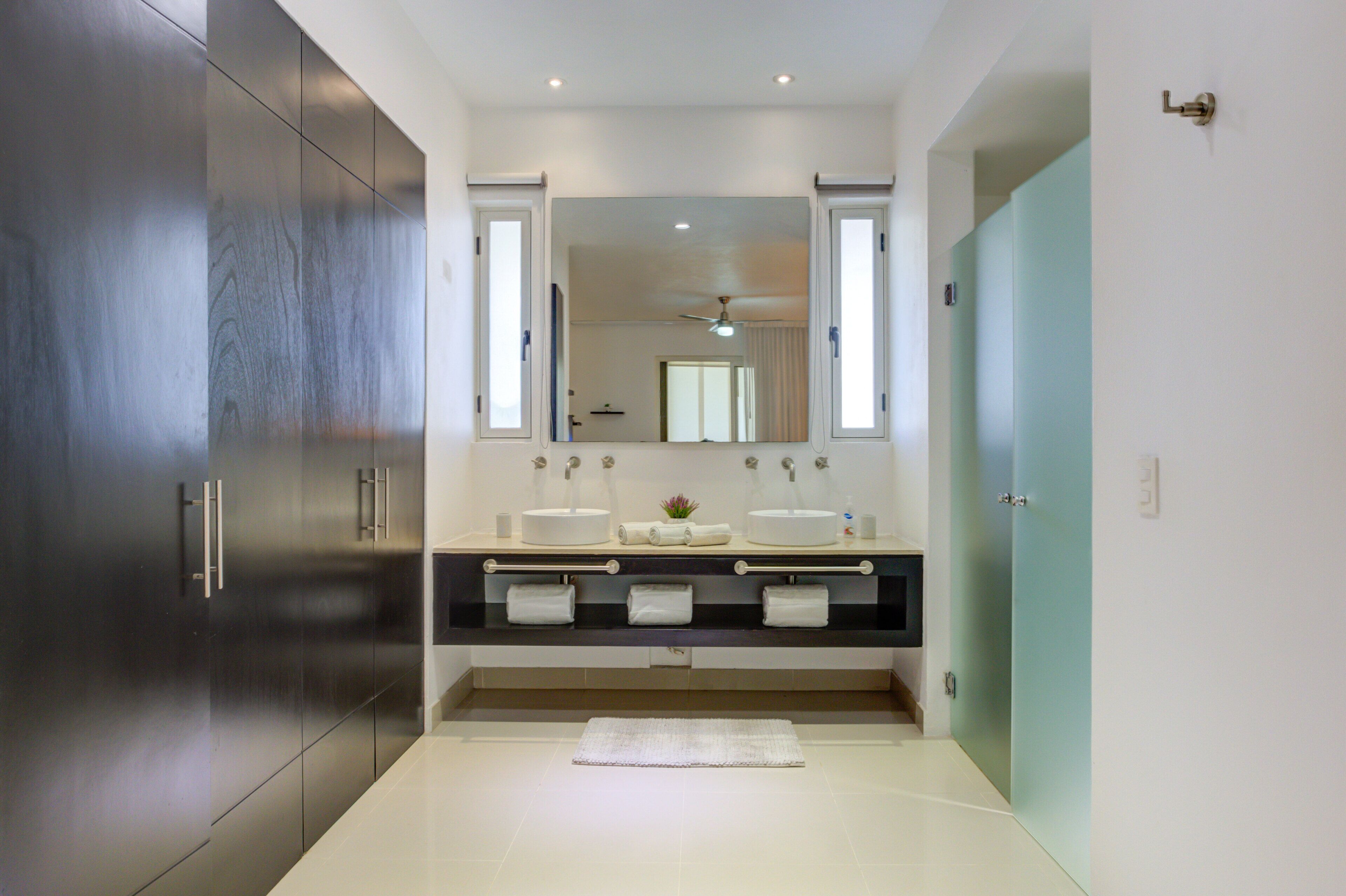 A modern bathroom with a large mirror, two sinks, a towel rack, and a dark wooden cabinet.