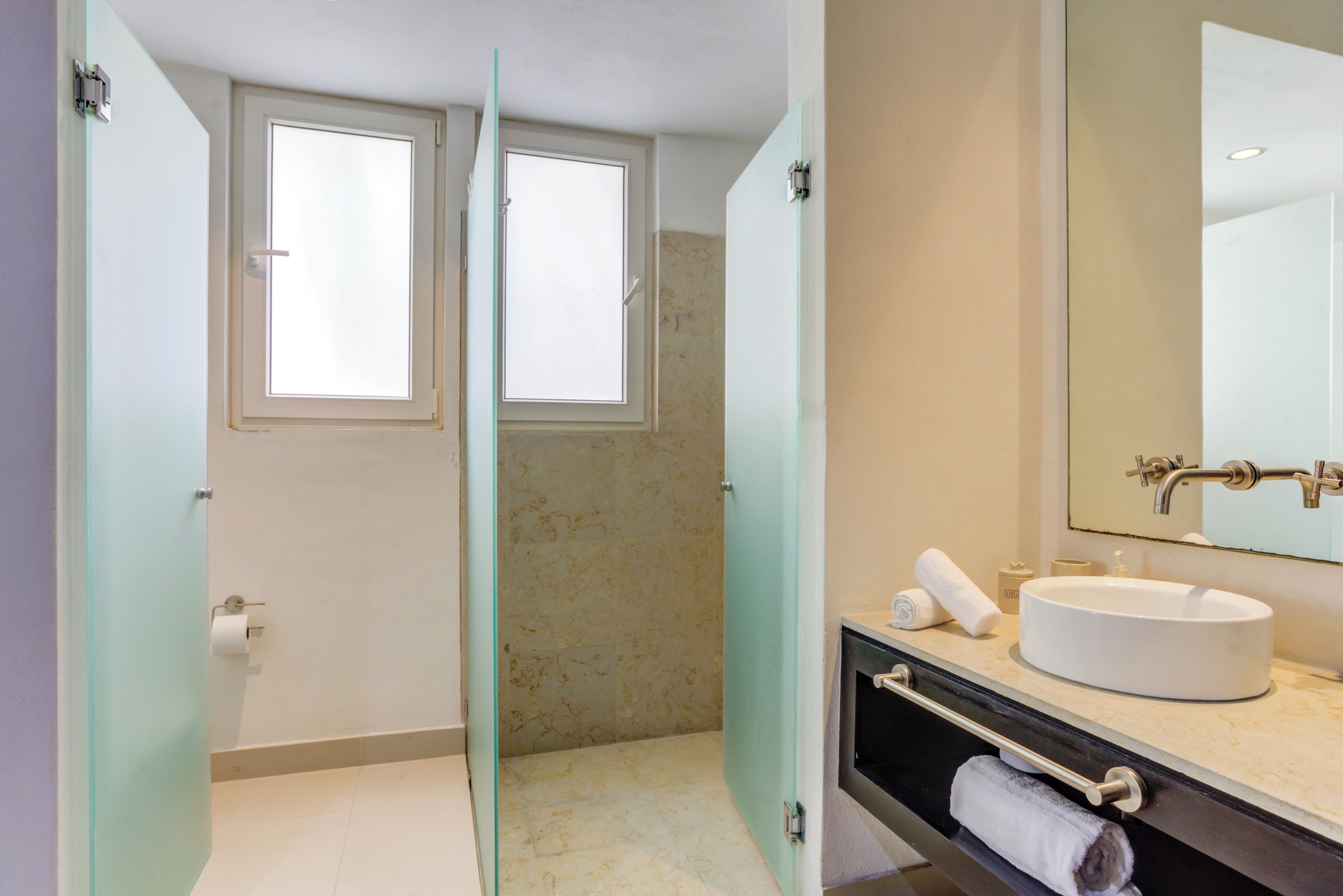 Un baño con puerta de cristal, un lavabo blanco, un espejo y un perchero para toallas.