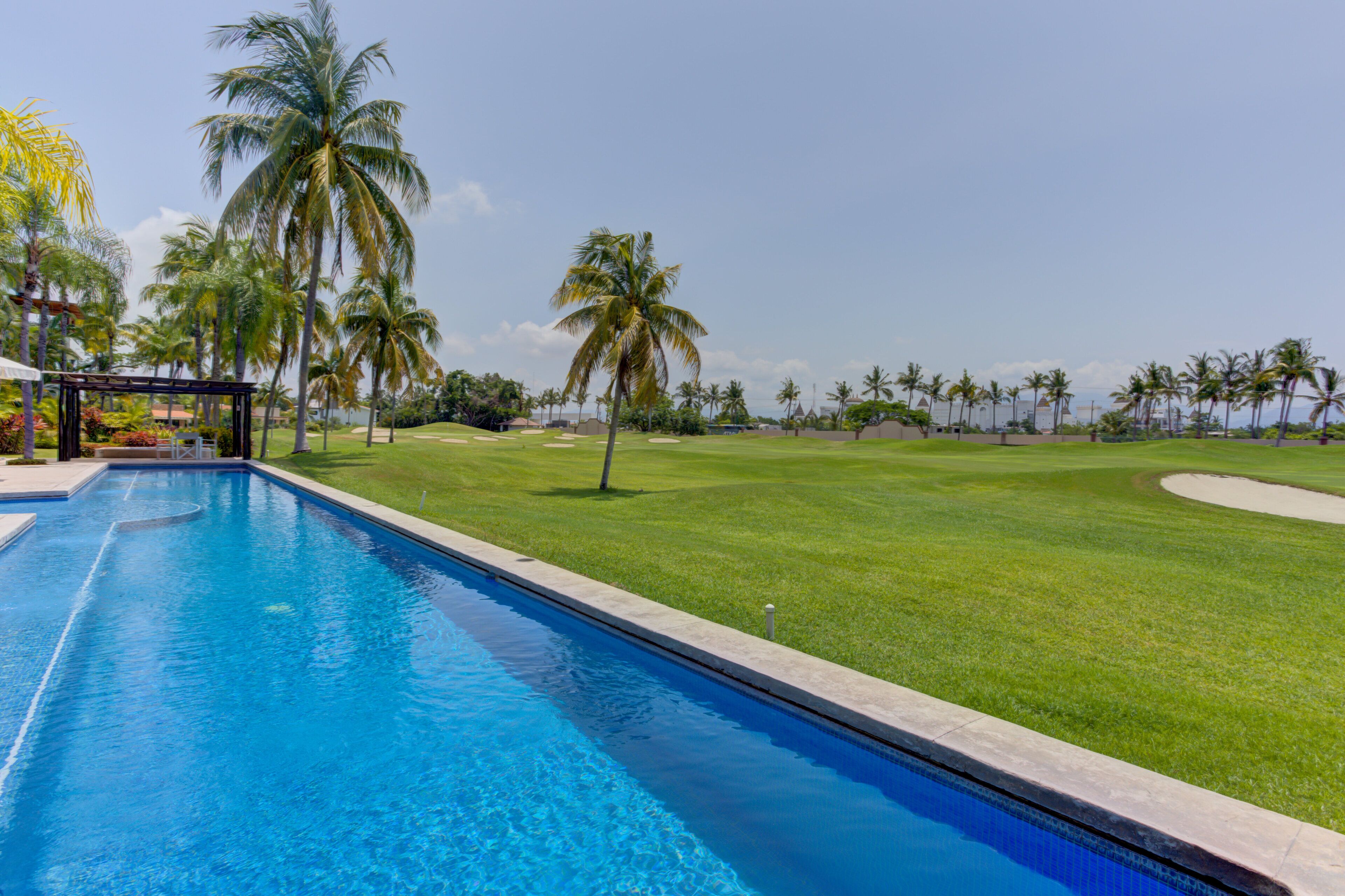 A swimming pool with a view of a golf course and palm trees.
