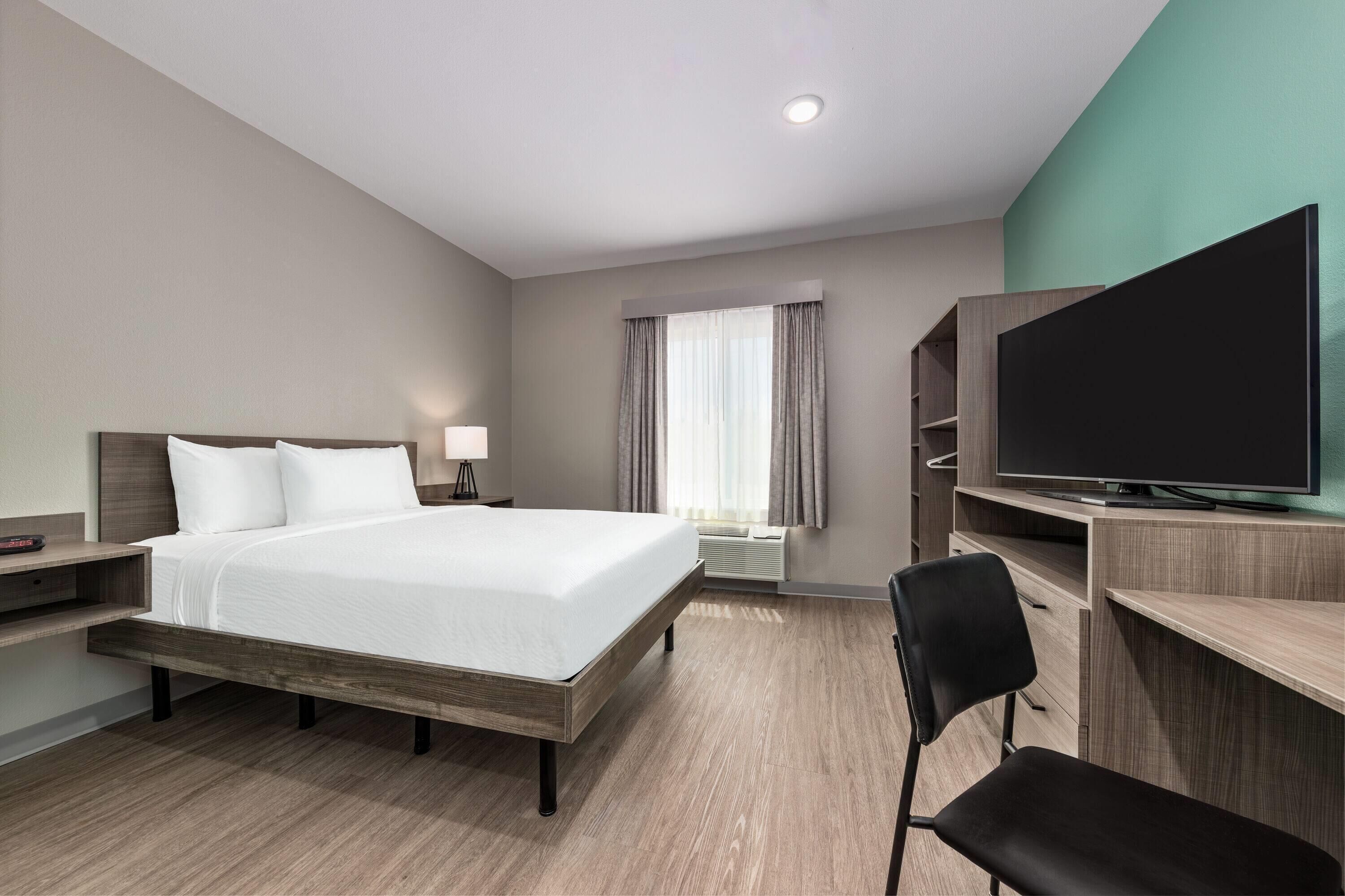 A hotel room with a bed, a TV, a desk with a chair, and a window with curtains.