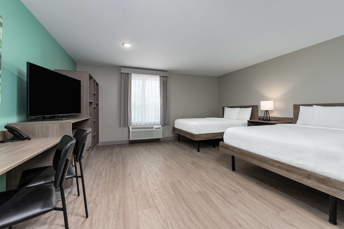 A hotel room with a desk, two beds, a TV, and a window with curtains.