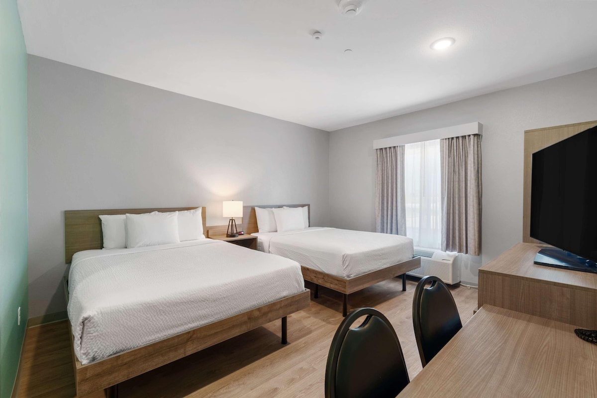 A hotel room with two single beds, a desk with a chair, a television, and a window with curtains.