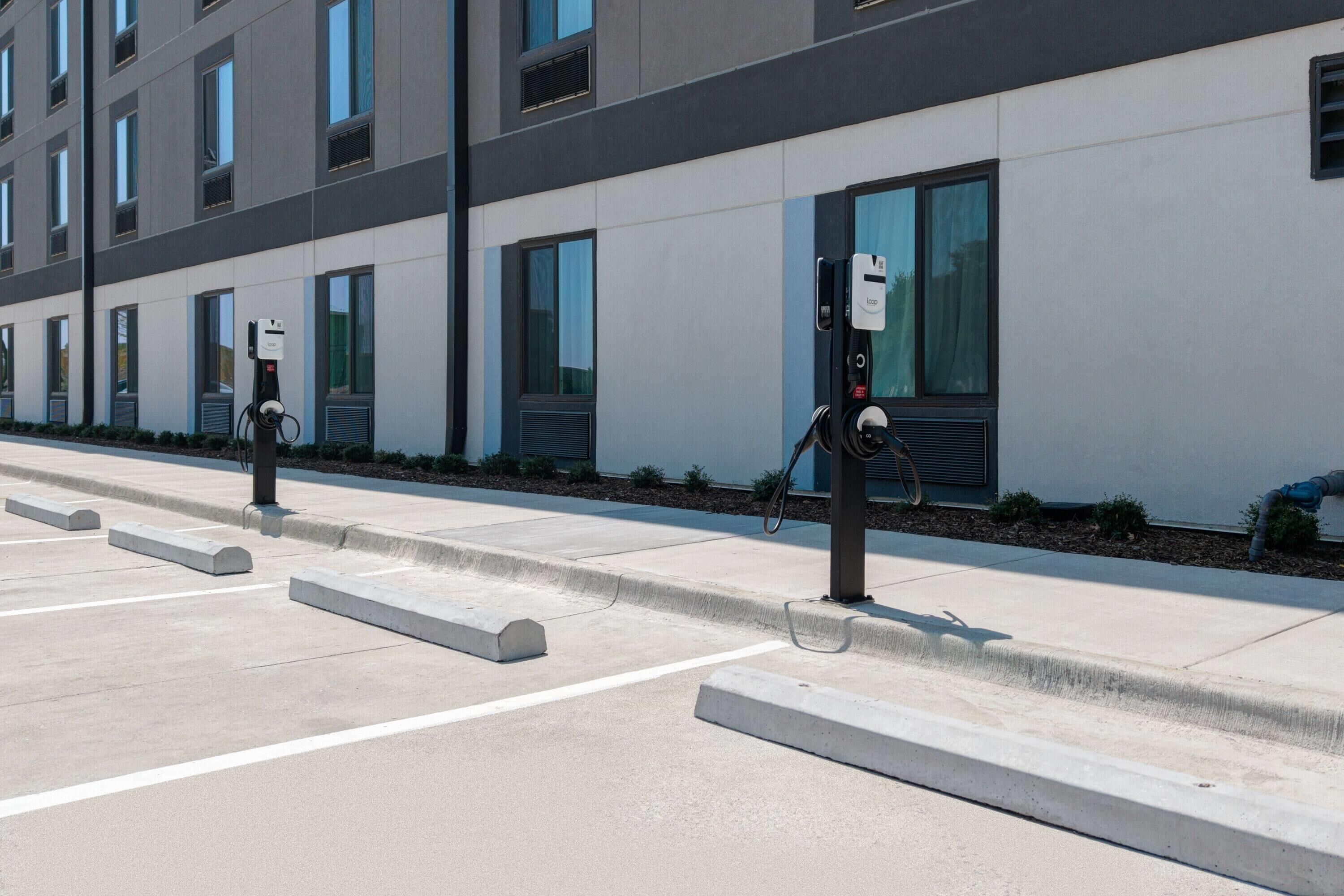 Een parkeerplaats met laadpalen voor elektrische voertuigen, een modern gebouw met grote ramen en een schoon, geplaveid oppervlak.