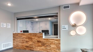 A reception area with a wooden reception desk, a check-in counter, and a wall-mounted sign indicating manager availability. - ECHO Suites Extended Stay by Wyndham Dallas Plano/Richardson (Plano)