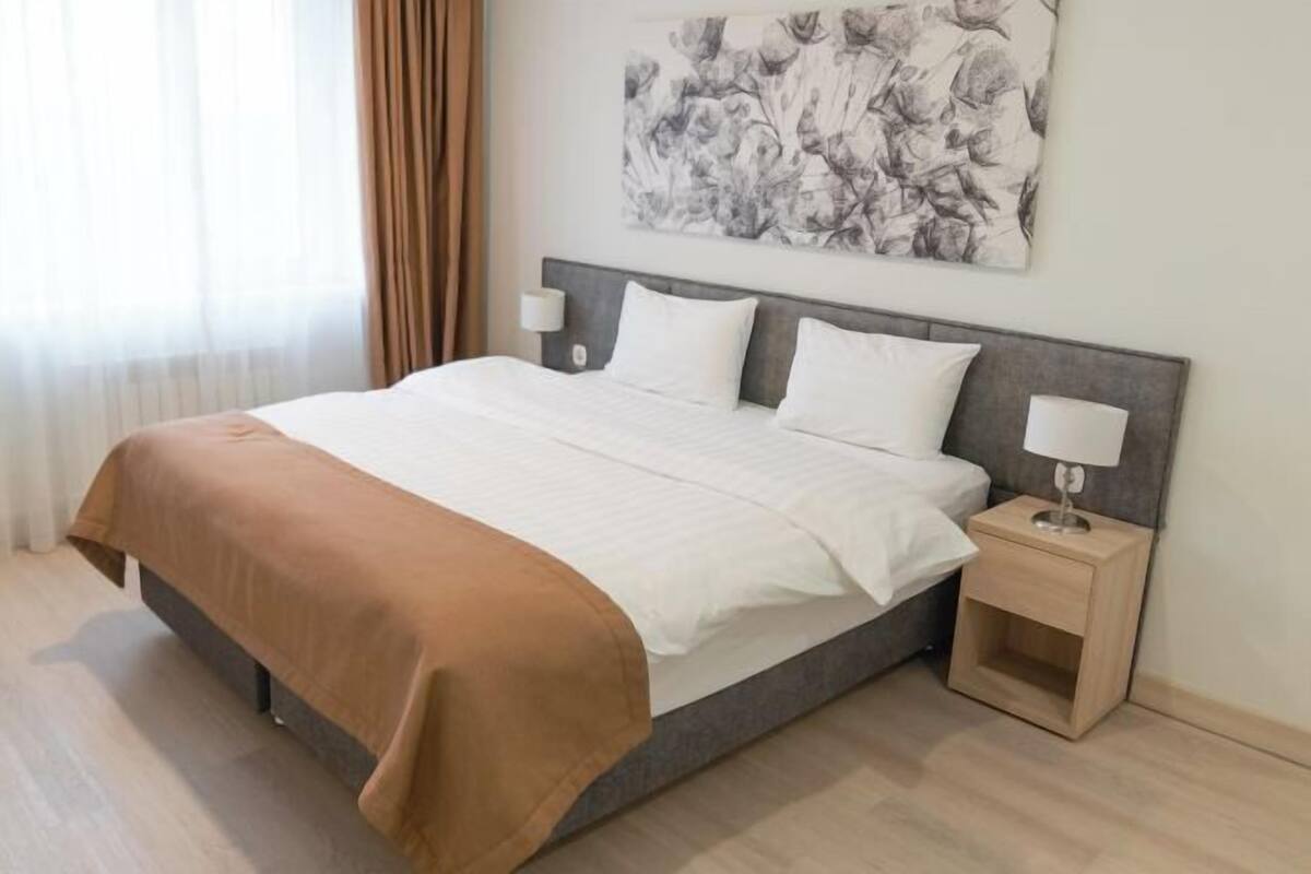 A neatly made bed with a brown bedspread, a headboard with a light fixture, and a wall-mounted artwork.