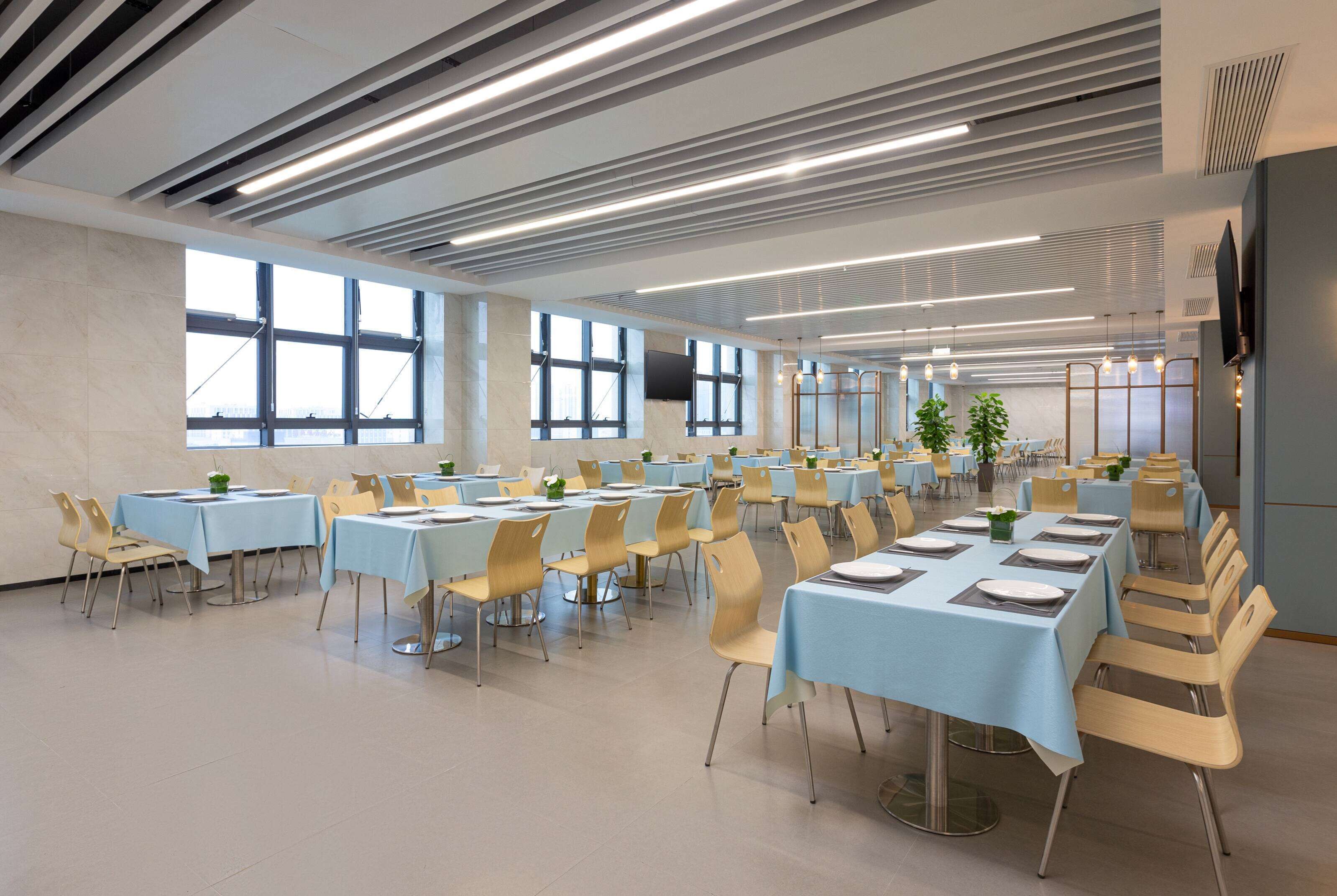A spacious conference room with multiple tables and chairs, large windows, and a modern ceiling design.