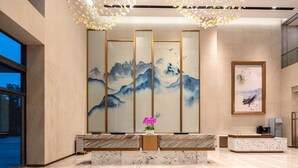 Un vestíbulo moderno con una recepción, un cuadro grande de montañas y un techo decorativo.