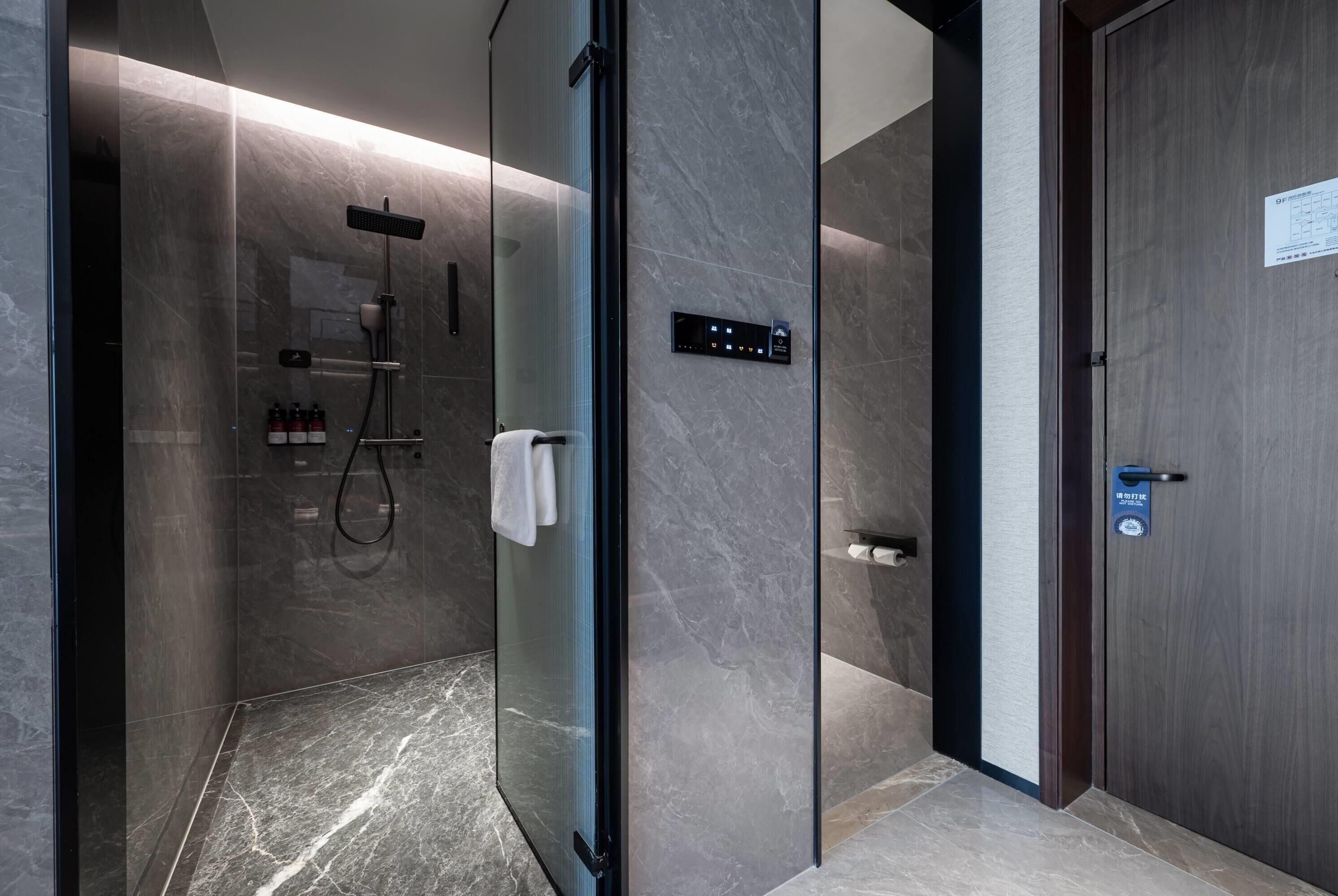A modern bathroom with a glass-enclosed shower, a control panel, and a wooden door.
