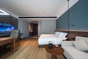 A modern hotel room with a bed, a desk, a chair, a coffee table, and a television.