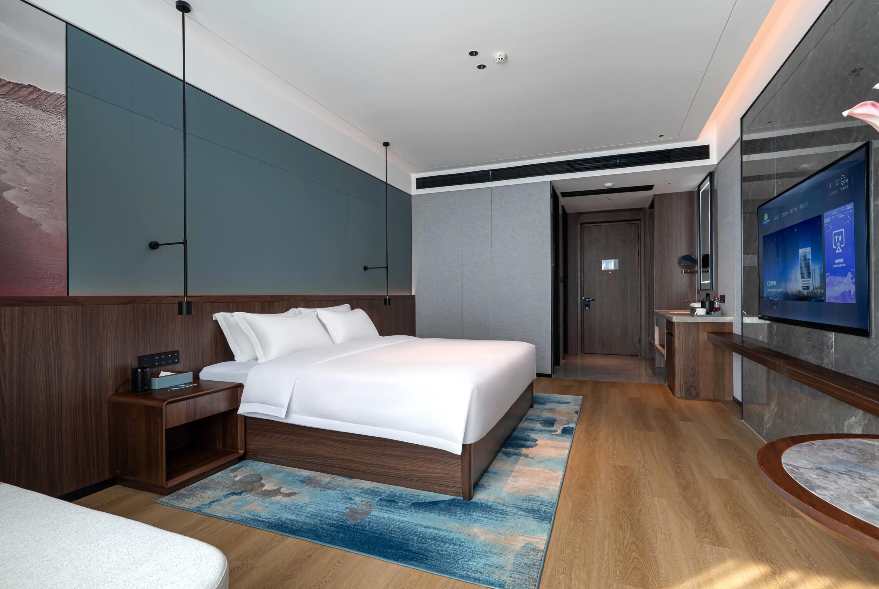 Een moderne hotelkamer met een groot bed, een bureau met een computer, een televisie en een badkamer zichtbaar door een open deur.