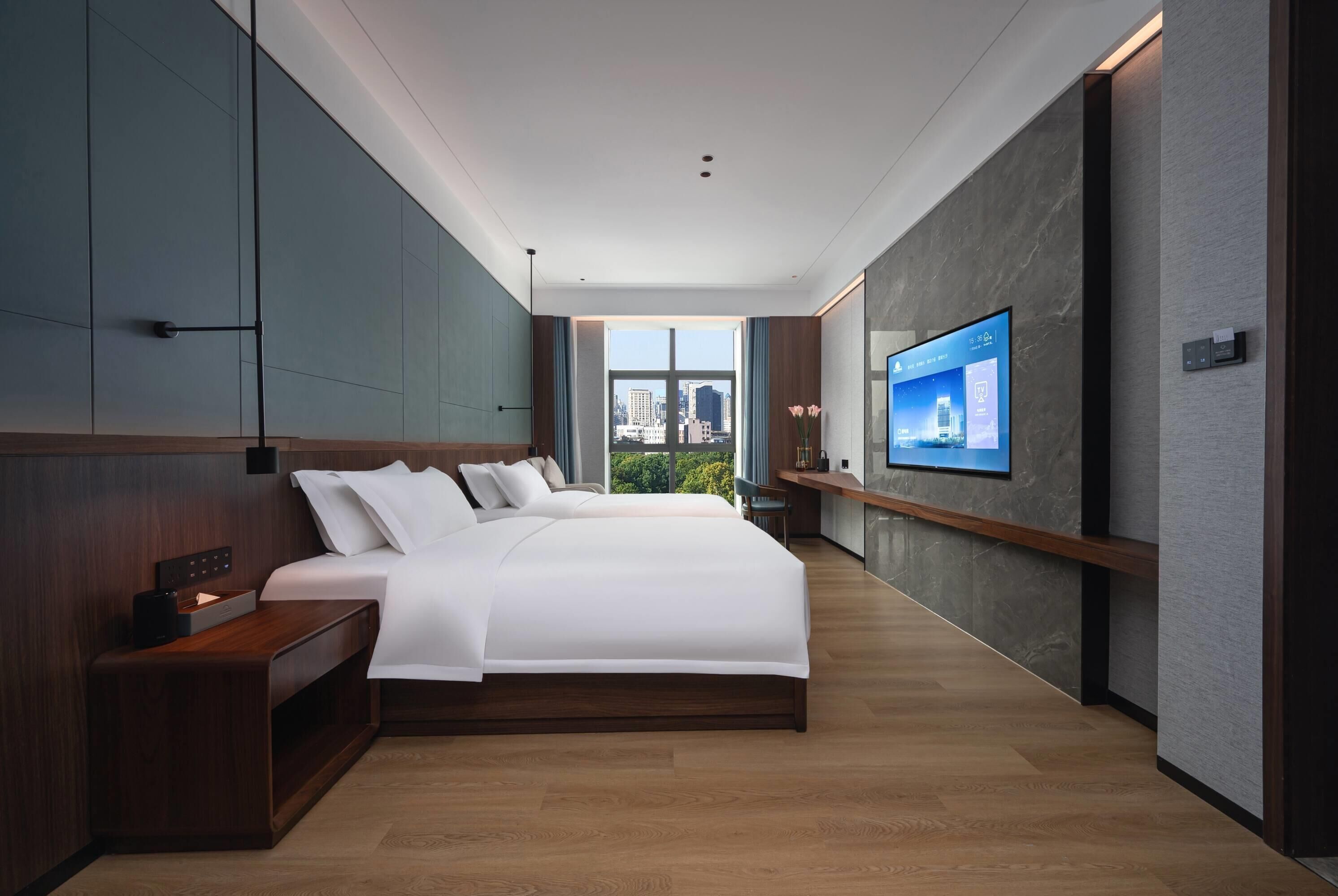 A modern hotel room with a large bed, a TV mounted on the wall, and a city view.