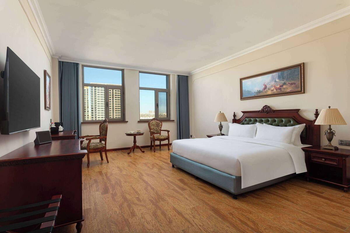 Habitación de hotel con una cama grande, un escritorio, una silla, un televisor y un cuadro en la pared.