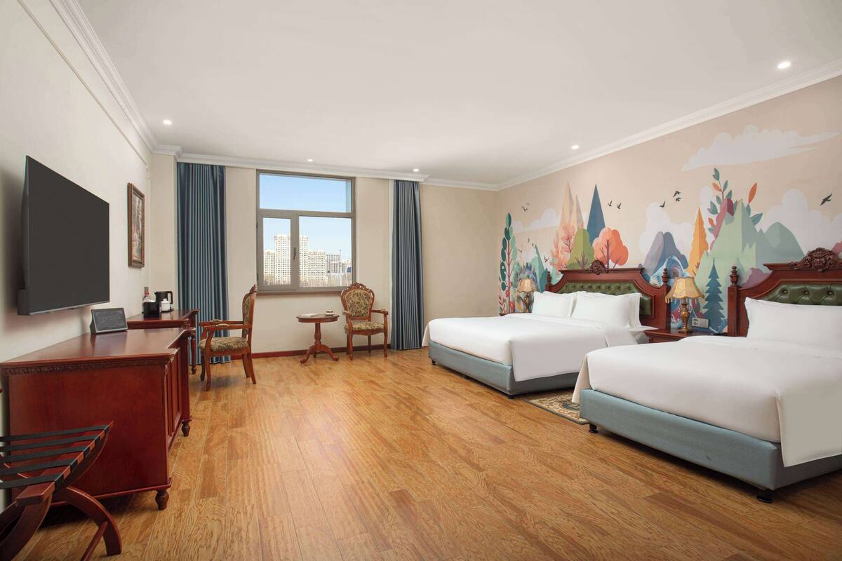 Habitación de hotel con dos camas, un escritorio con silla, un televisor y ventana con vista a la ciudad.