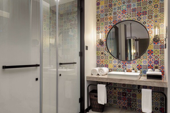 A bathroom with a glass shower enclosure, a tiled backsplash, a round mirror, and a sink with towels. - Days Inn By Wyndham Harbin Qunli (Harbin)