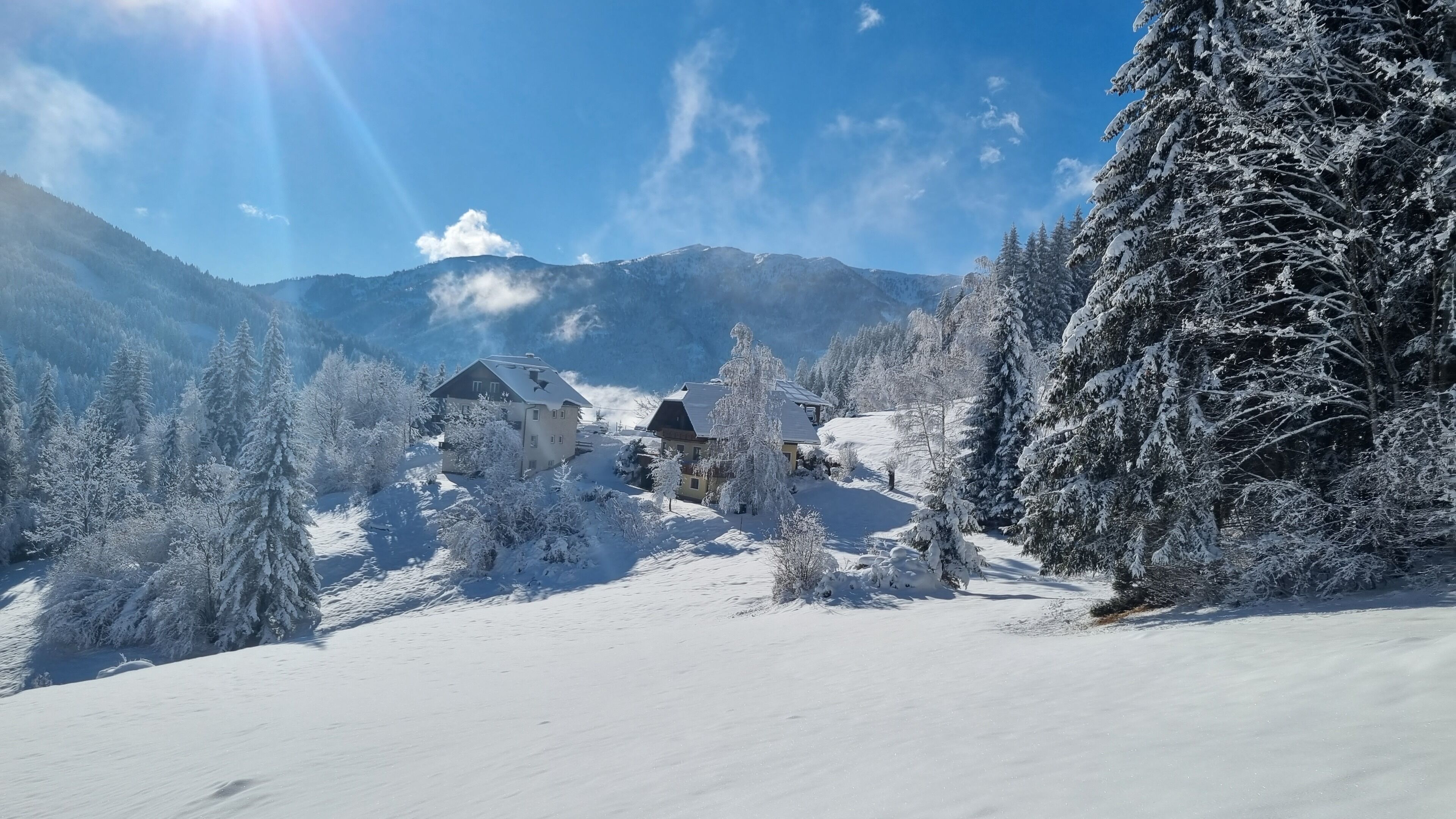 Paisagem coberta de neve com uma casa rodeada por árvores e montanhas.