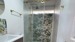 A bathroom with a glass-enclosed shower, a white toilet, and a wooden vanity.