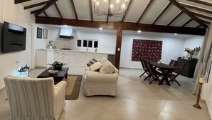 A spacious living area with a high ceiling, a dining set, a sofa, and a TV mounted on the wall.