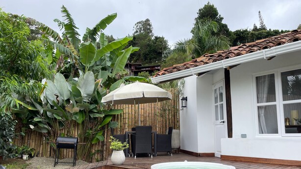 A patio area with a hot tub, outdoor furniture, and lush greenery.