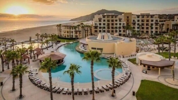 Un resort con piscina central, palmeras y vista a la playa.