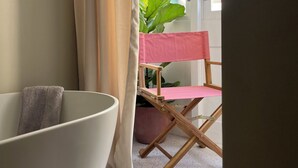 A room with a white bathtub, a wooden chair with a pink cover, and a large green plant. - Charming studio with WiFi and AC in enchanting Il-Furjana (Il-Furjana)