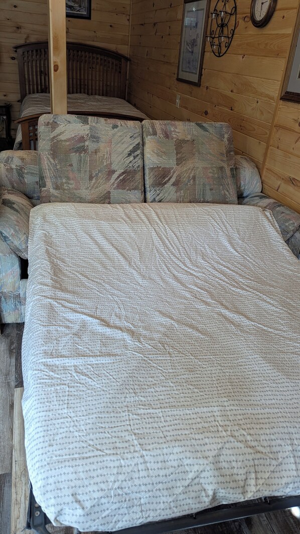 A bed with a patterned quilt, a wooden headboard, and a wall clock.