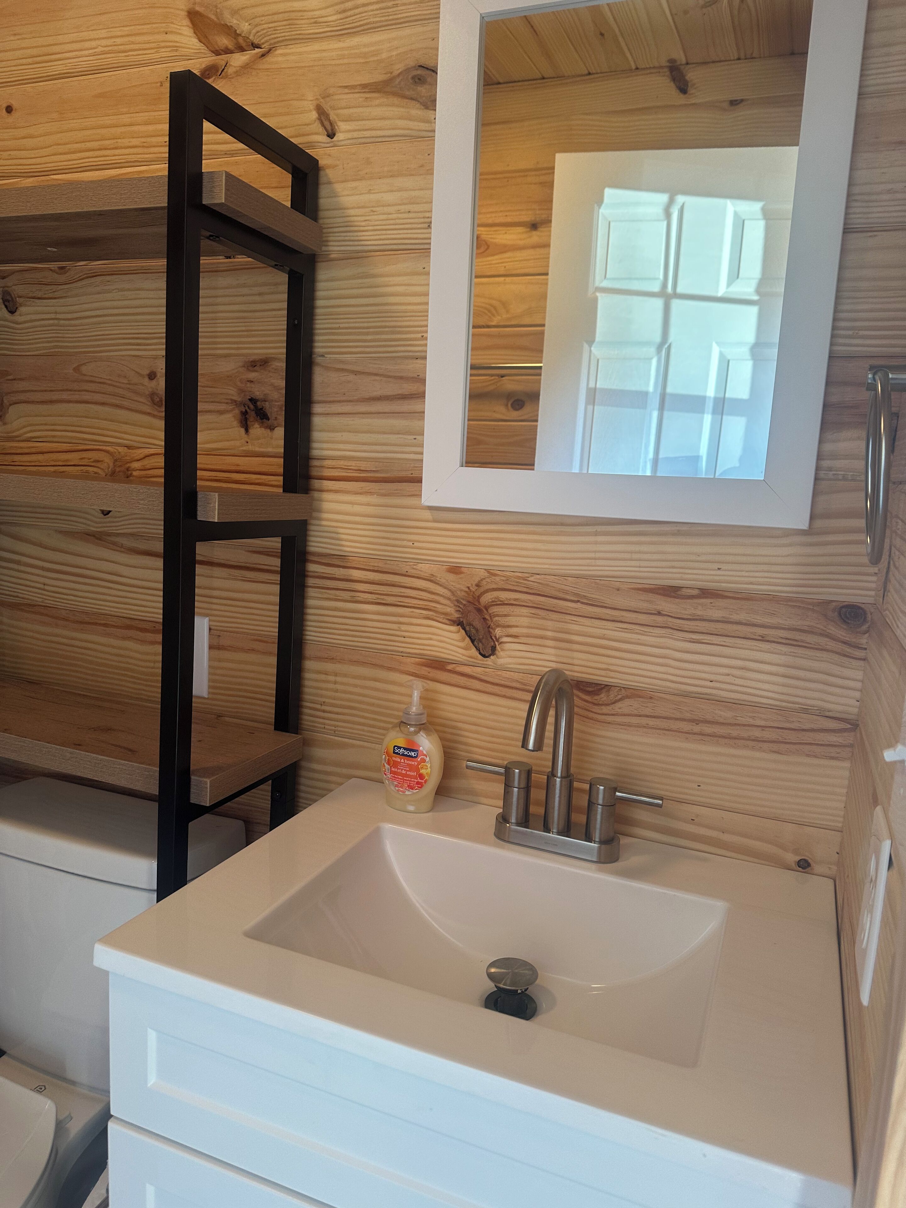 A bathroom with a wooden wall, a white sink, a mirror, and a soap dispenser.