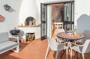 Une terrasse extérieure avec une table ronde, des chaises blanches, un barbecue et un four à pizza.