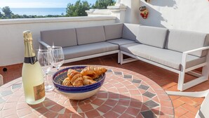 A terrace with a white sofa, a table with a bowl of croissants, a bottle of champagne, and two glasses. - Las Palmas 20c - El Oasis de Capistrano (Nerja)