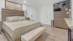 A bedroom with a bed, a bench, a dresser, a TV, and a painting on the wall. - Tropical Delight Studio Suite (Atlanta)