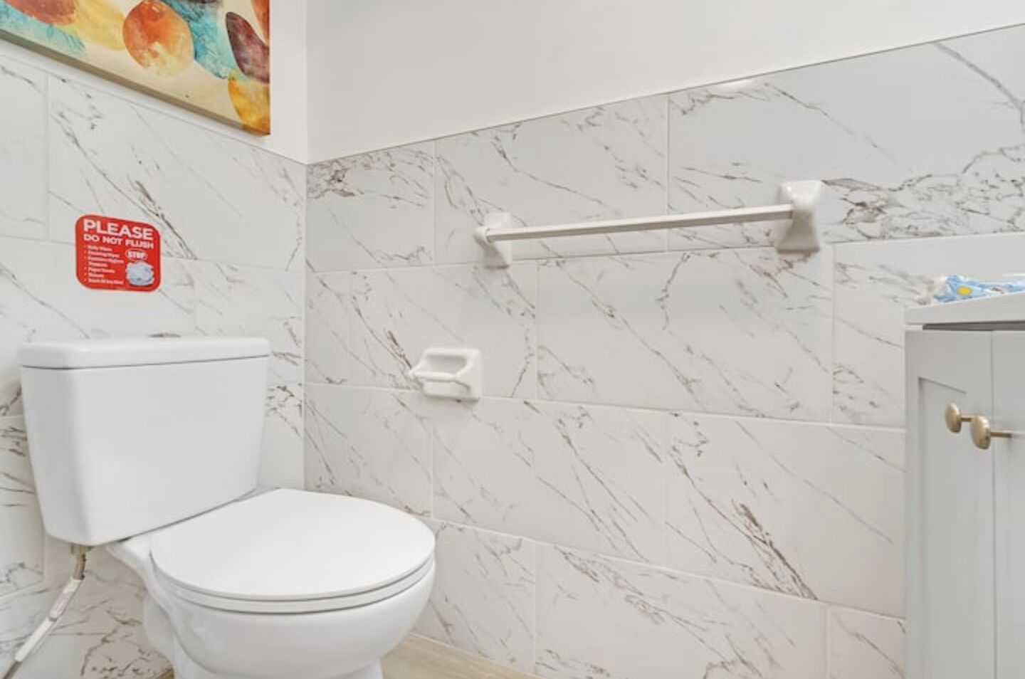 A bathroom with a toilet, a hand dryer, and a marble wall.