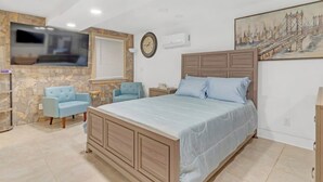 A bedroom with a bed, a TV mounted on the wall, a clock, and a painting. - Bahama Mama Studio Suite (Atlanta)