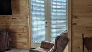 Een blokhut interieur met een houten vloer, een bank met bloemenprint, een houten stoel en een televisie aan de muur.