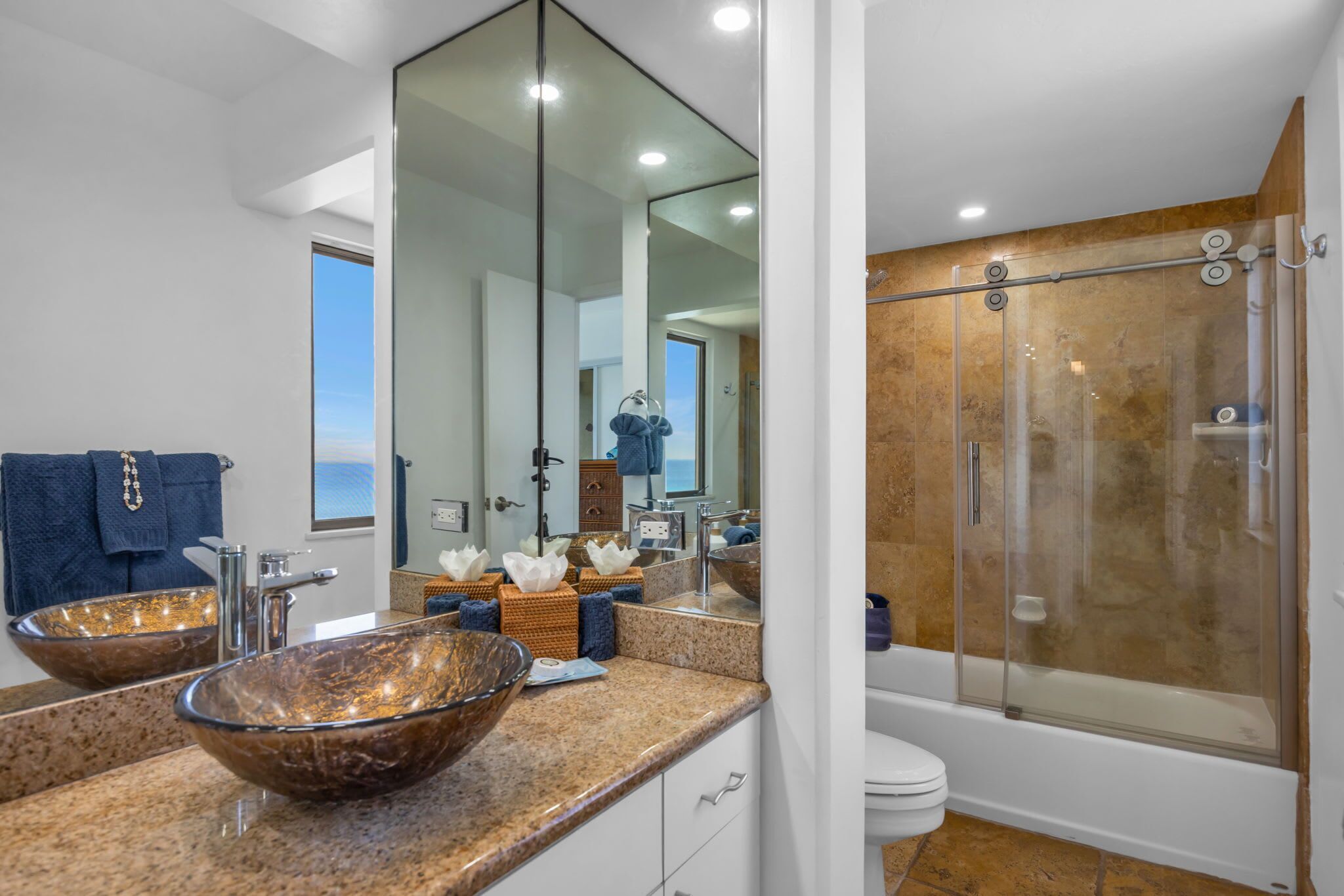 Un baño moderno con un espejo grande, dos lavamanos, una cabina de ducha de vidrio y vistas al océano.