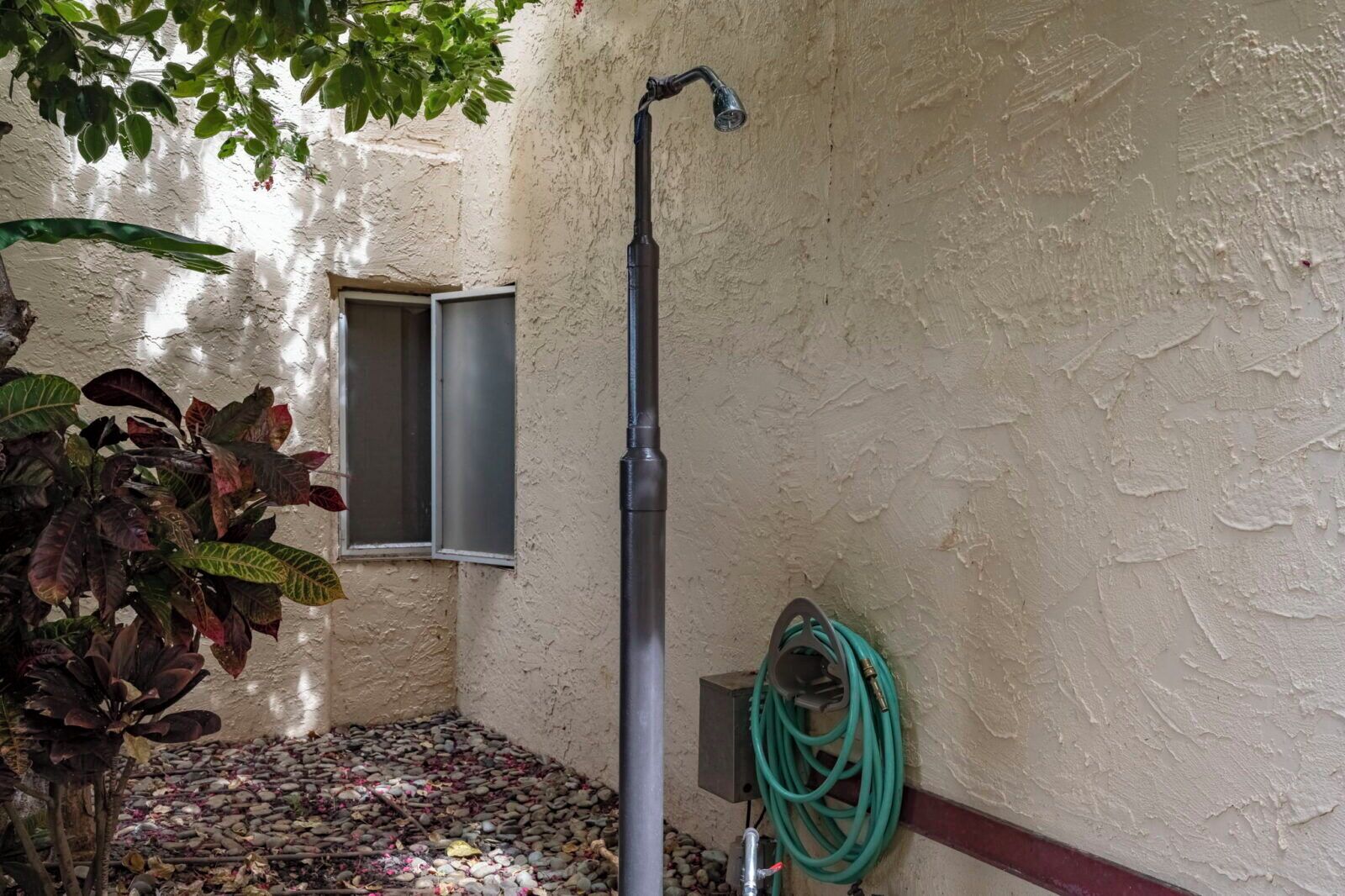 Ein kleiner Außenbereich mit einem Brunnen, einem Gartenschlauch und einem Fenster.