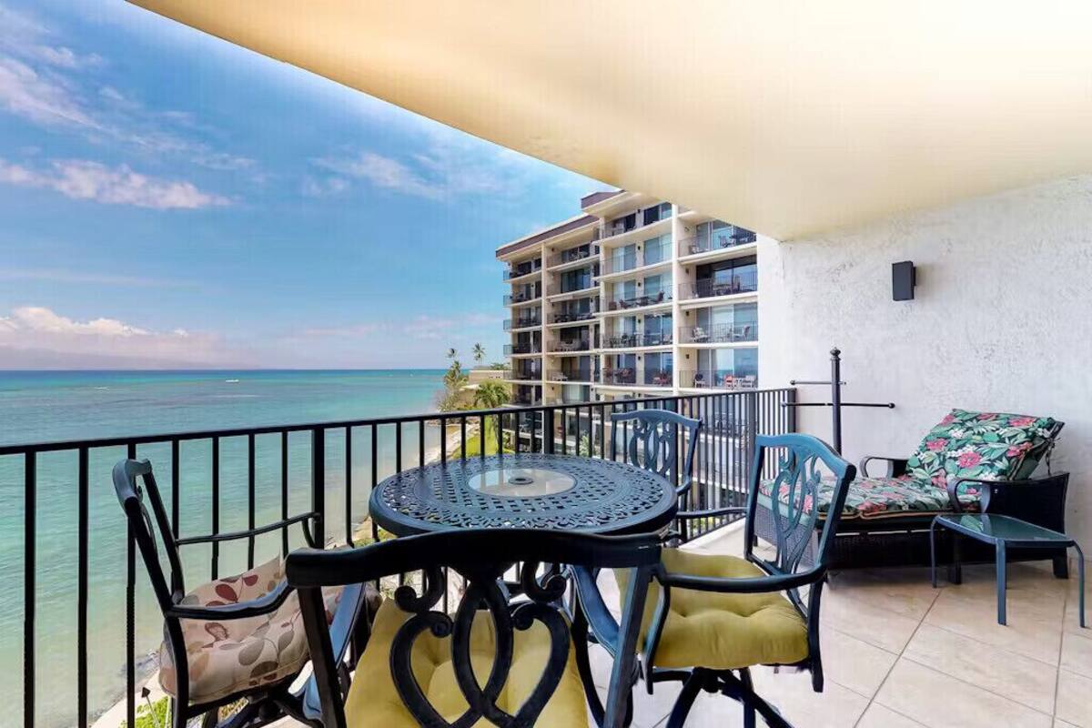 A balcony with a table and chairs, overlooking a body of water and a building.