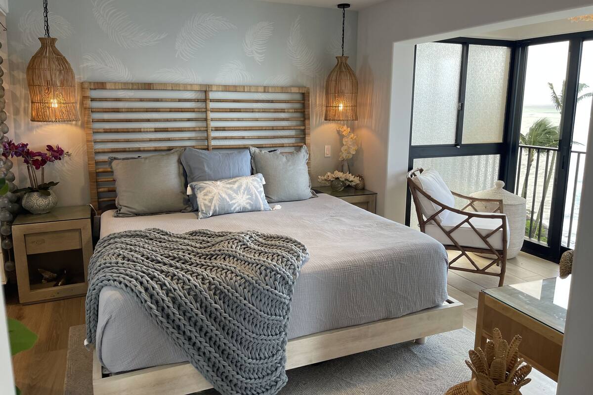 A bedroom with a bed, bedside tables, a chair, a window with a view, and hanging lamps.