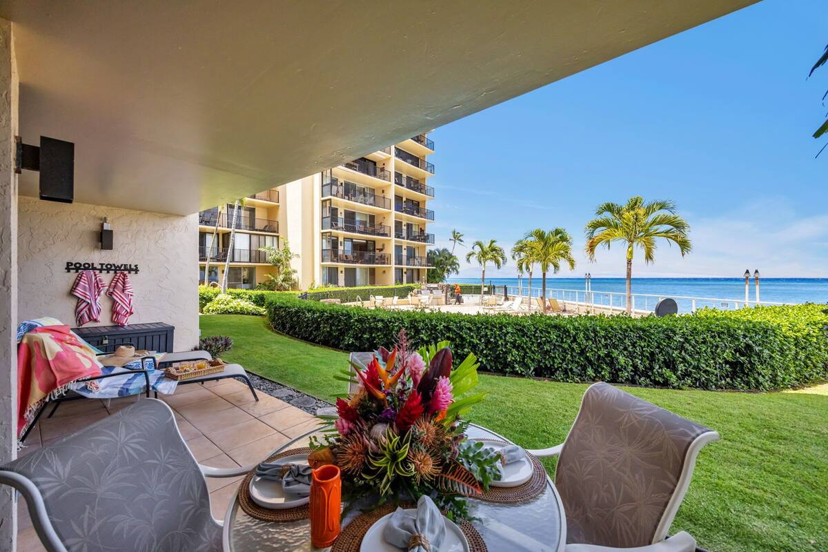 A patio with a table set for two, a decorative plant, and a view of the ocean.