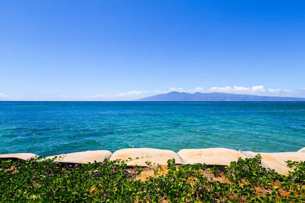 Une vue sur la côte, avec un ciel dégagé, une mer calme et des montagnes à l’horizon.